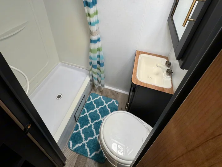 Functional RV rental bathroom with a white shower, toilet, sink vanity, and a pop of color from the teal mat.. Keystone RV Springdale 2022