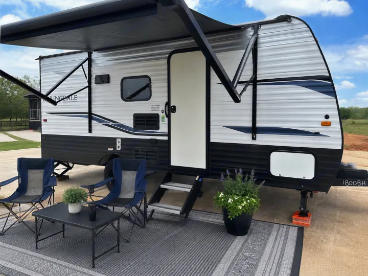 This RV rental features a comfortable outdoor setup with an extended awning, camping chairs, and a small table.. Keystone RV Springdale 2022