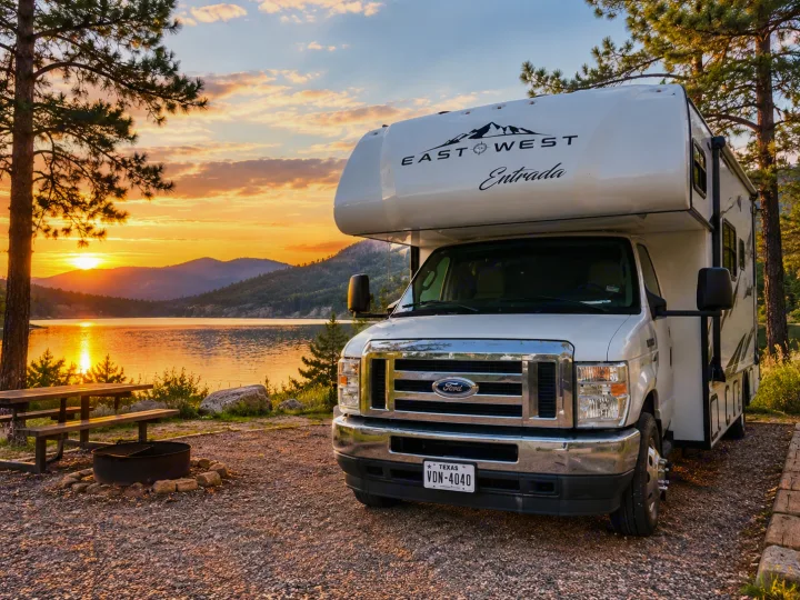 Enjoy an RV rental adventure! This East West Entrada Class C RV is parked at a beautiful lakeside campsite at sunset.. East to West Entrada 2024