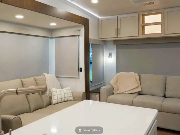 Experience comfort in this modern RV rental living area, featuring light-toned sofas, window blinds, and overhead storage.. Alliance RV Avenue 2026