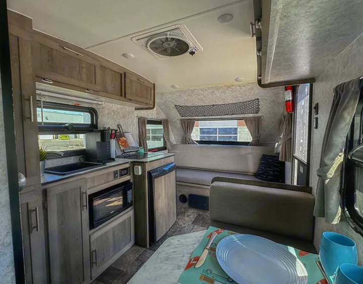 Inside this RV rental: a compact kitchen with sink, microwave, and fridge, plus a cozy dinette and overhead storage.. Prolite Lounge 2022