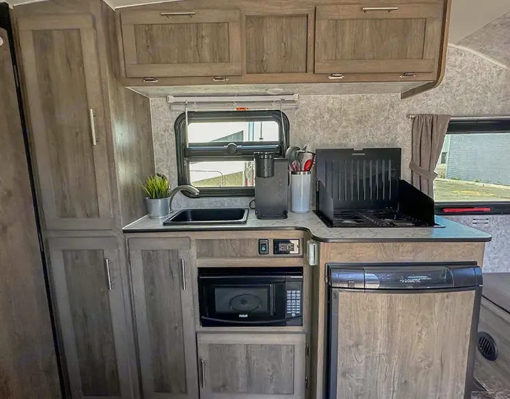 This RV rental features a compact kitchen with a sink, stove, microwave, fridge, and ample storage.. Prolite Lounge 2022