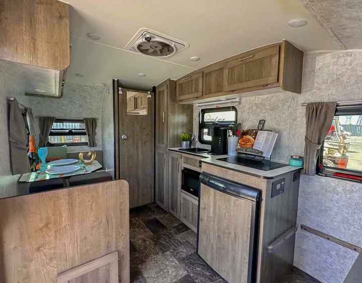 View inside an rv rental, showing a well-equipped kitchen, dining table set for two, and overhead cabinets.. Prolite Lounge 2022