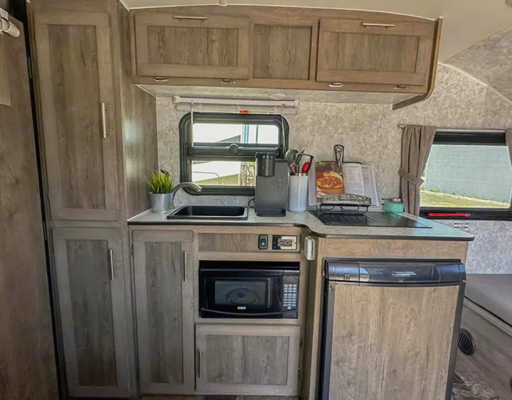 This RV rental kitchen features a compact sink, stove, microwave, fridge, and wood-grain cabinets, perfect for mobile cooking.. Prolite Lounge 2022