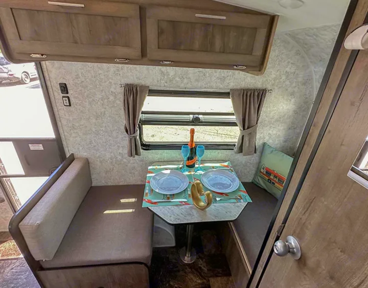 Cozy rv rental dinette with booth seating, a table set for two, and overhead cabinets for storage.. Prolite Lounge 2022