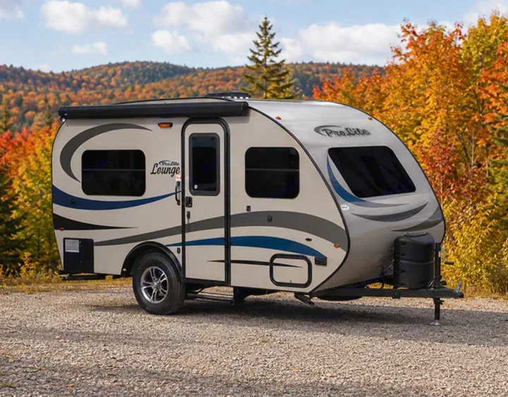 A compact ProLite Lounge travel trailer RV rental, parked on gravel, with vibrant autumn trees in the background.. Prolite Lounge 2022