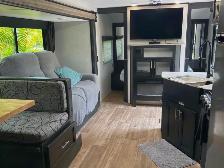Interior of an RV rental: living area with sofa & dining, modern kitchen, and entertainment center with TV/fireplace.. Forest River Cherokee 2022
