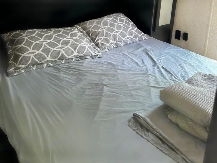 Comfortable bed in an RV rental, featuring gray sheets, two patterned pillows, and neatly folded extra linens.. Forest River Cherokee 2022