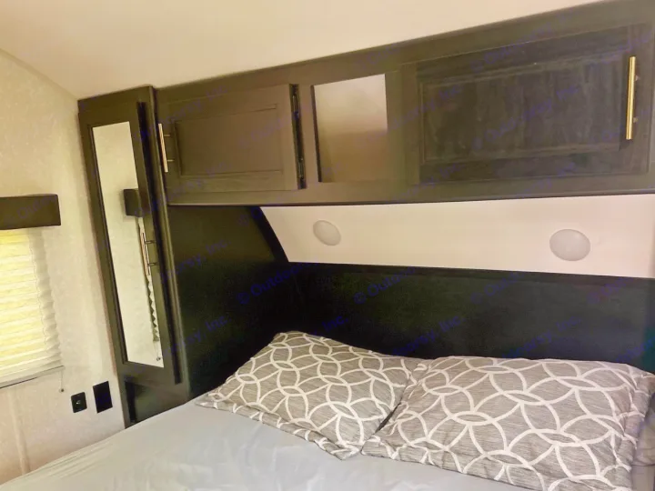 Cozy RV rental bedroom: dark overhead cabinets, mirrored wardrobe, and patterned pillows on a grey bed, offering storage and comfort.. Forest River Cherokee 2022