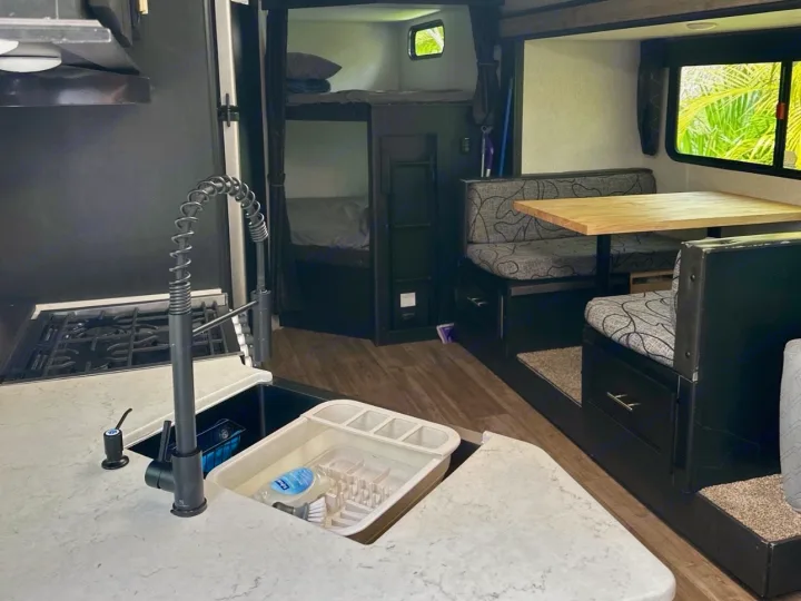 Inside an rv rental: kitchen with black faucet, dinette with wood table, and bunk beds for comfort.. Forest River Cherokee 2022