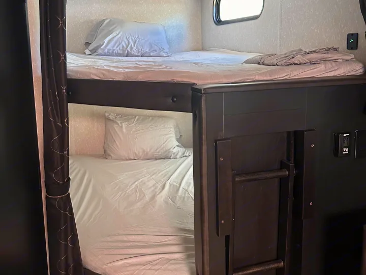 RV rental interior featuring a set of dark bunk beds with fresh white linens, a window, and dark privacy curtains.. Forest River Cherokee 2022