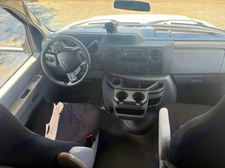 RV rental: Inside a Ford van cab. Dashboard with steering wheel, basic radio, and cup holders. Front seats visible.. Coachmen Freelander Freelander 2022