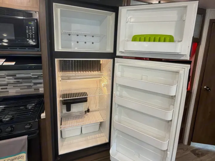 RV rental kitchen: open fridge/freezer, green ice mold, microwave, and stovetop visible in compact camper interior.. Keystone RV Cougar 2019