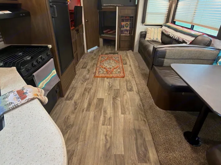 Inside this RV rental: kitchen with stove, comfy dinette, and bunk beds. A well-equipped camper for trips.. Keystone RV Cougar 2019