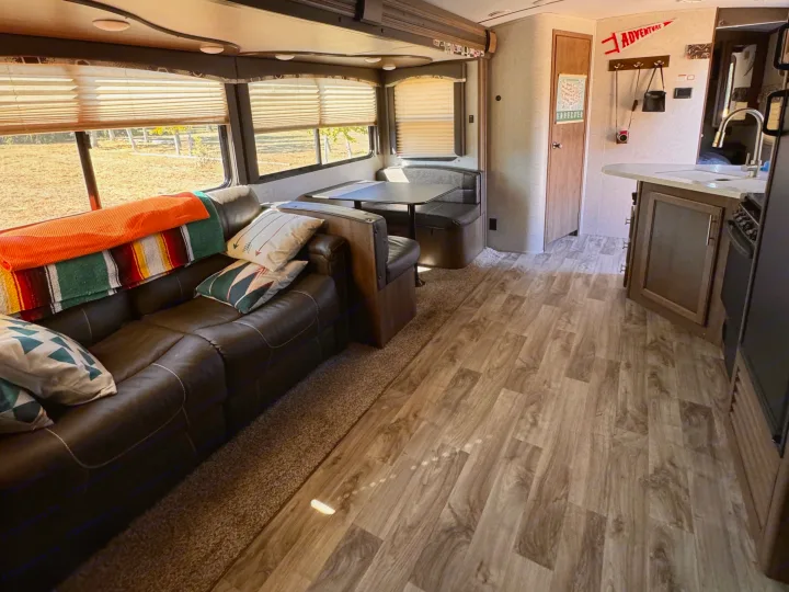 RV rental interior: A cozy living space with a dark leather sofa, dining area, and wood-look flooring leading to the kitchen.. Keystone RV Cougar 2019