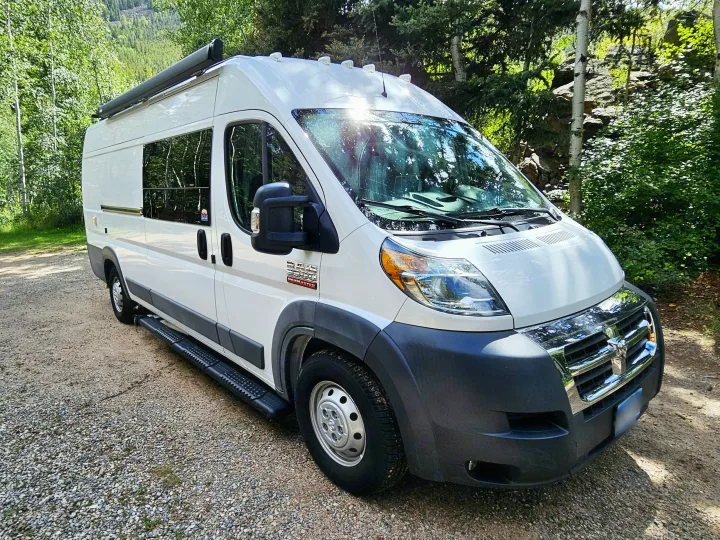 White Ram ProMaster camper van RV rental parked on a gravel road amidst green trees, ideal for your next outdoor trip.. Dodge Ram ProMaster 3500 2018