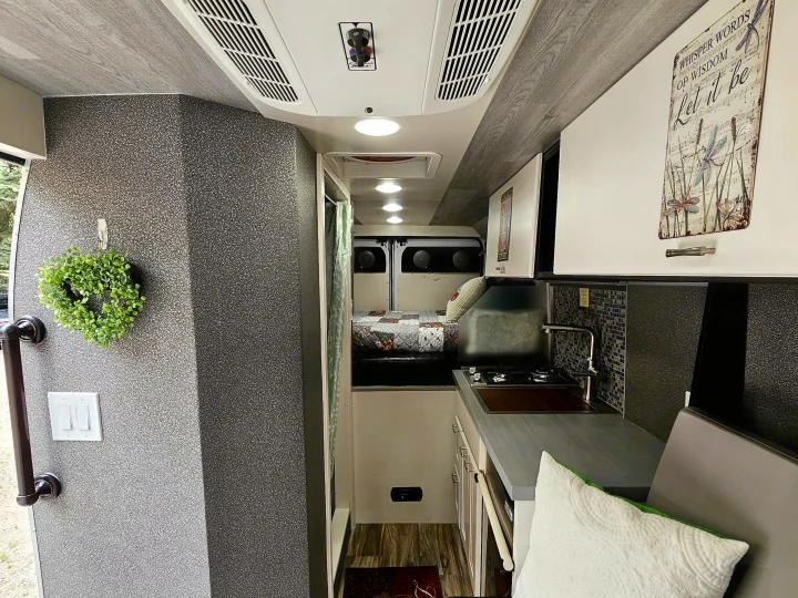 Cozy RV rental interior: kitchenette, bed, seating, and AC unit, offering a complete living space.. Dodge Ram ProMaster 3500 2018
