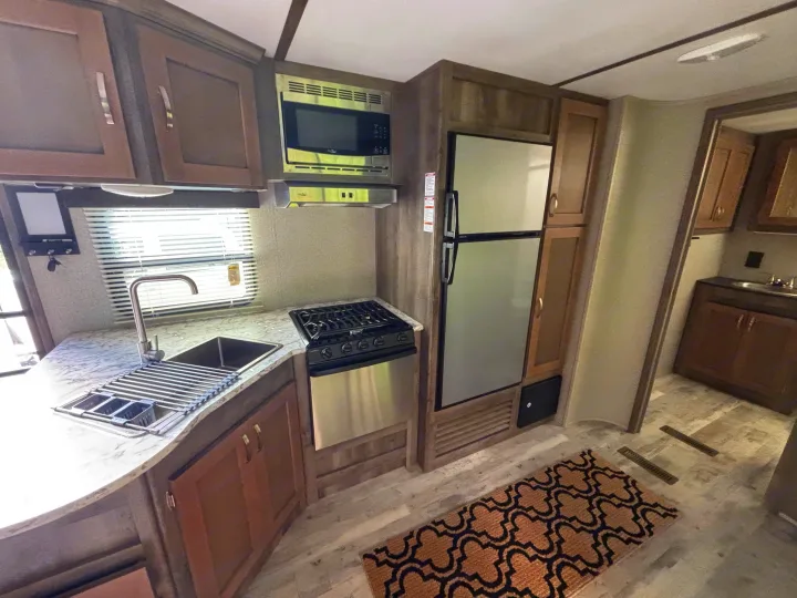 Well-appointed RV rental kitchen interior featuring stainless microwave, stove, fridge, large sink, and ample cabinet space.. Keystone RV Sprinter Campfire Edition 2018