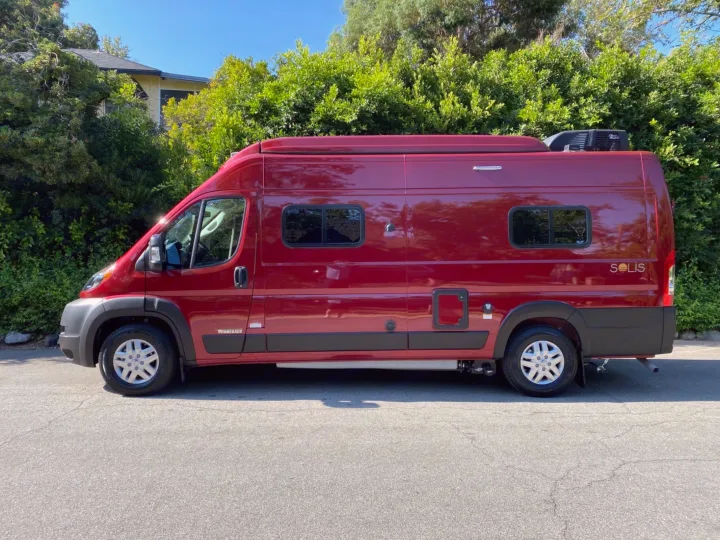 This vibrant red Winnebago Solis camper van, ideal for rv rental, is parked outdoors on a sunny day with green trees.. Winnebago Solis 2024