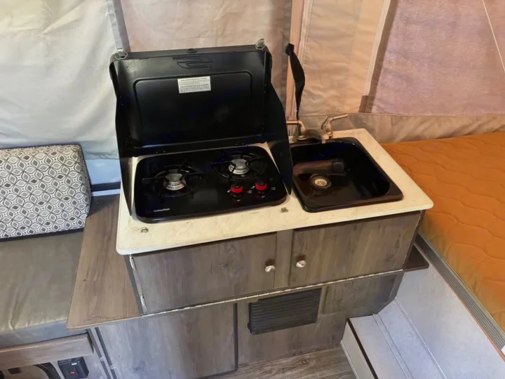 Inside an RV rental: a compact kitchen featuring a two-burner stove, sink, and wood-grain cabinets.. Coachmen clipper 2020