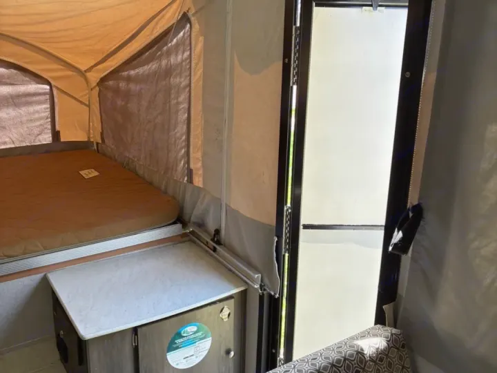 Inside this RV rental pop-up camper: a bed with a brown mattress, a small counter, and the entry door on the right.. Coachmen clipper 2020