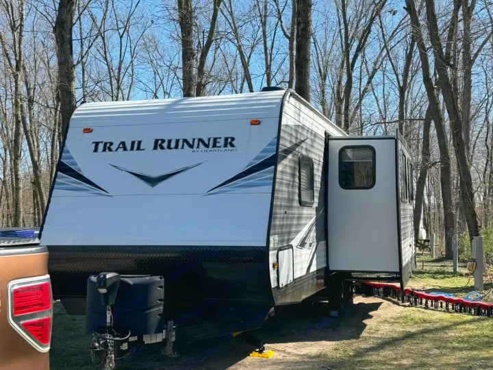 This rv rental, a Trail Runner travel trailer, is set up at a wooded campsite, ready for outdoor adventures.. Heartland RVs Trail Runner 2021