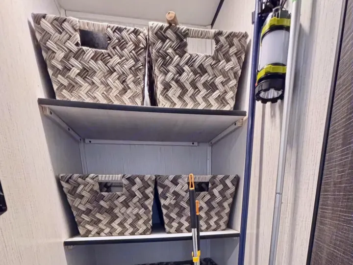 Maximizing space in an rv rental! This organized closet has shelves with woven baskets, cleaning essentials like a vacuum & broom.. Heartland RVs Trail Runner 2021