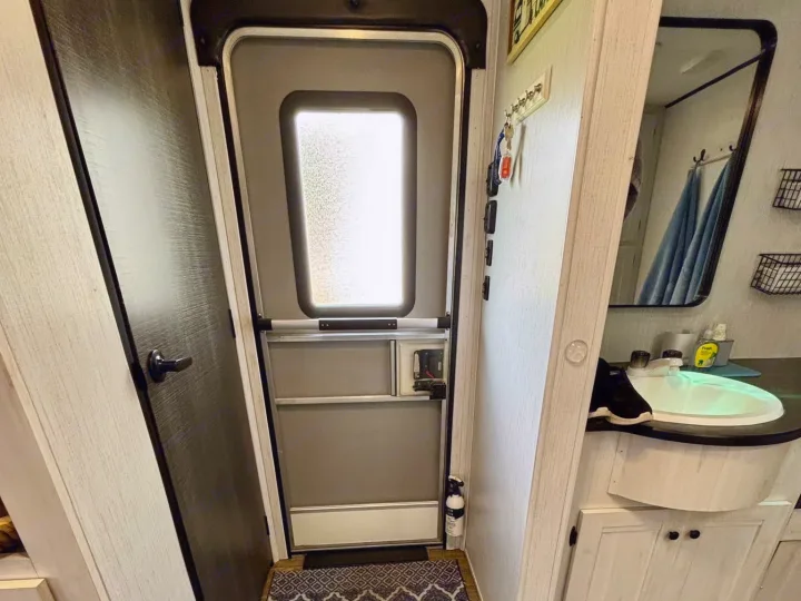 RV rental interior showing an entry door, a small bathroom vanity, and two rugs on wood-look flooring. Practical layout.. Heartland RVs Trail Runner 2021