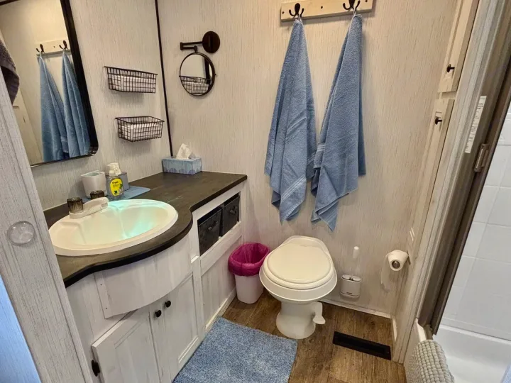 Compact RV rental bathroom features a small vanity with sink, toilet, shower, and blue accents. Functional interior.. Heartland RVs Trail Runner 2021