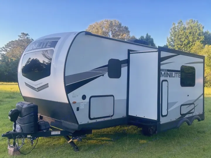 Light gray travel trailer with an open slide-out, parked in a grassy field. Ideal for an rv rental adventure.. Rockwood Mini Lite 2104S 2023