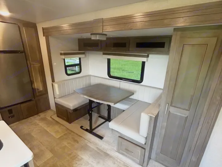 RV rental interior: U-shaped dinette, table, windows with greenery, fridge, and cabinets. Cozy space for travel.. Rockwood Mini Lite 2104S 2023