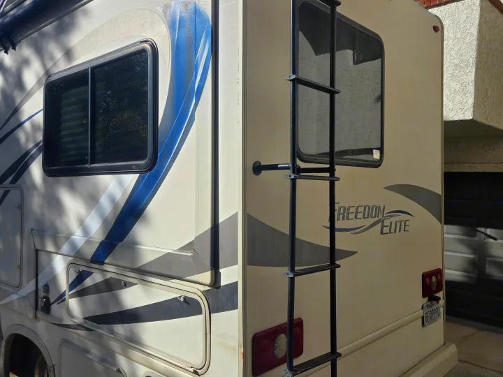 Cream-colored Freedom Elite rv rental motorhome with a ladder, parked outdoors. Perfect for your next road trip adventure.. Thor Freedom Elite 2019