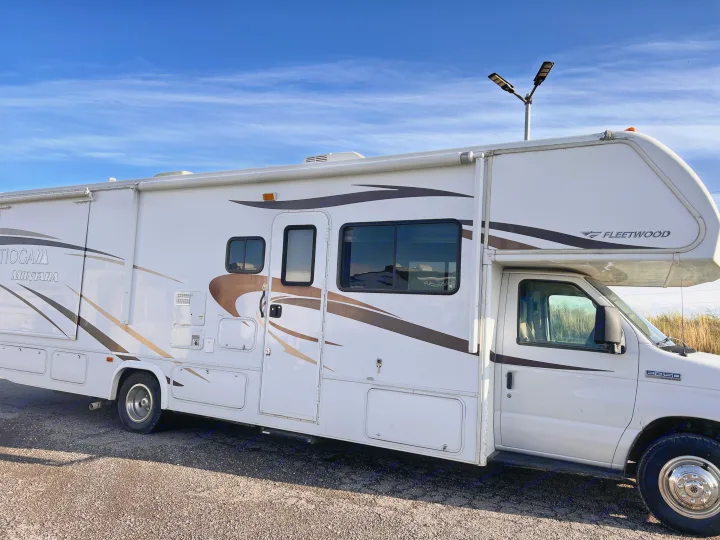 White Fleetwood Tioga Montara Class C RV with brown decals, parked outside under a blue sky. Perfect for an rv rental.. Tioga Montara 2013