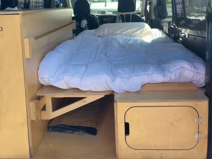 Inside a customized RV rental van: a comfy bed and built-in wooden storage, perfect for road trips.. Ram Promaster City 2018