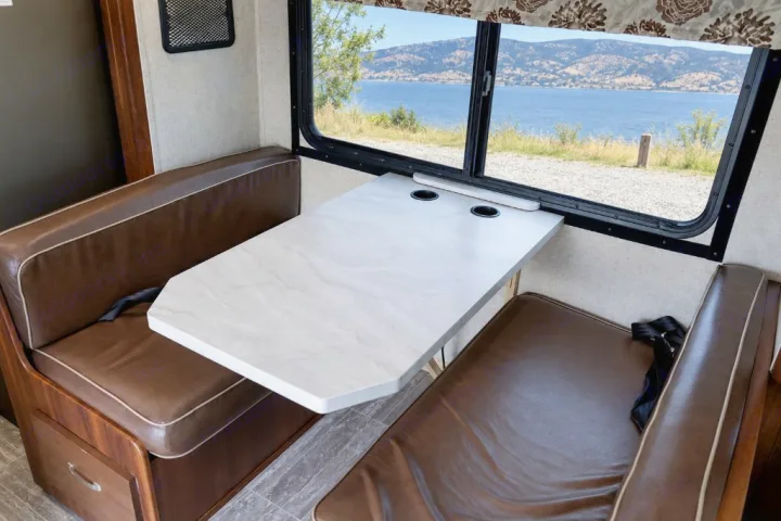 RV rental interior: dining area with brown upholstered benches, a light marble-look table with cupholders, and a scenic lake view.. Forest River Forester 2020