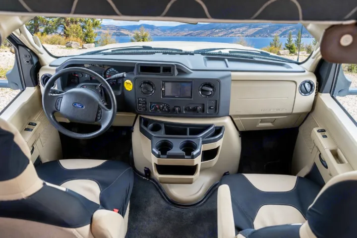 RV rental cockpit: dashboard, Ford steering wheel, seats, and cup holders, with a scenic lake view through the windshield. Ready for travel.. Forest River Forester 2020
