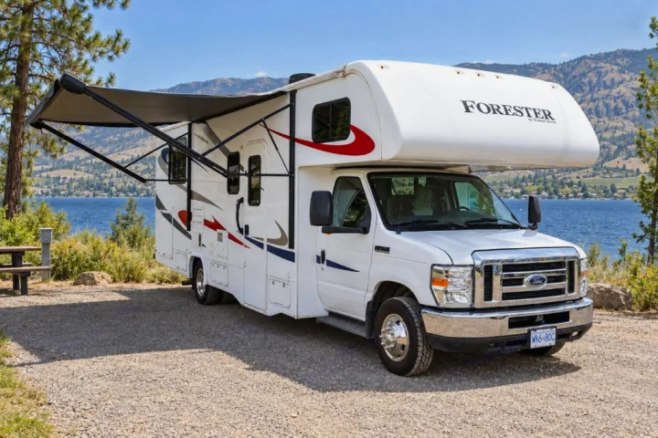 This spacious RV rental offers lakeside camping with an extended awning. A white Forester motorhome on gravel by mountains.. Forest River Forester 2020