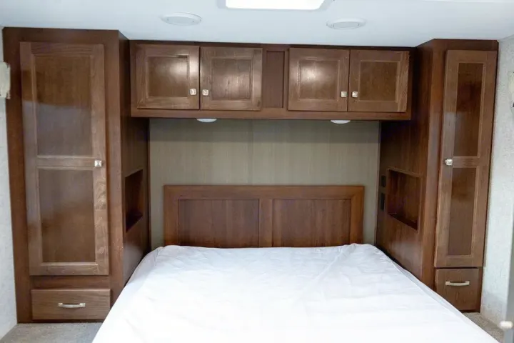 RV rental bedroom featuring a comfortable bed, wooden headboard, and ample overhead & side storage cabinets.. Forest River Forester 2020