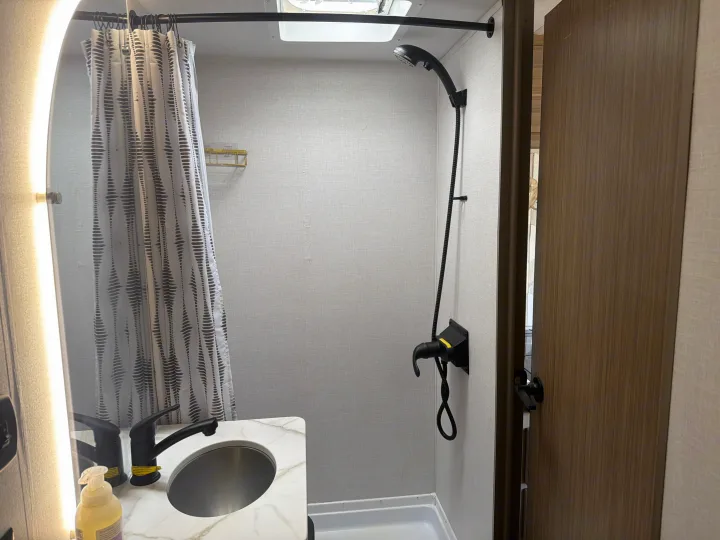 An RV rental bathroom features a compact vanity, black faucet, patterned shower curtain, and a black wall-mounted shower system.. Forest River Salem FSX 2026