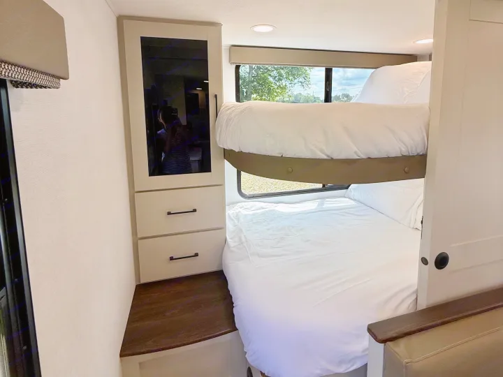 This RV rental bunk bed area features a mirrored wardrobe, drawers, and windows with white bedding for comfort.. Alliance Delta 2027