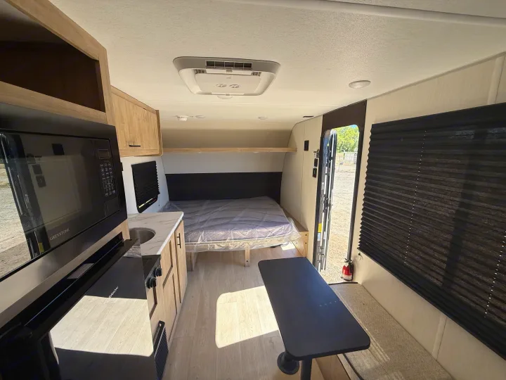 Inside a clean RV rental: kitchen with microwave & sink, bed with plastic cover, and dining table with bench seating.. Forest River Cherokee Wolf Pup 2026
