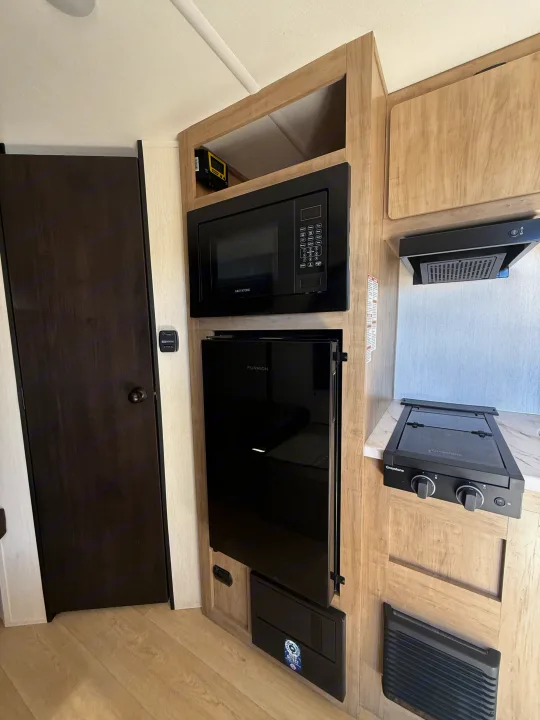 Interior view of an RV rental kitchen with Greystone microwave/stove, Furrion fridge, range hood, and light wood cabinets.. Forest River Cherokee Wolf Pup 2026