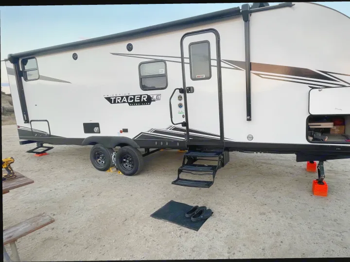 RV rental: A white travel trailer is set up with leveling blocks and steps on a sandy campsite, ready for adventure.. Forest River Prime Time LE 2023