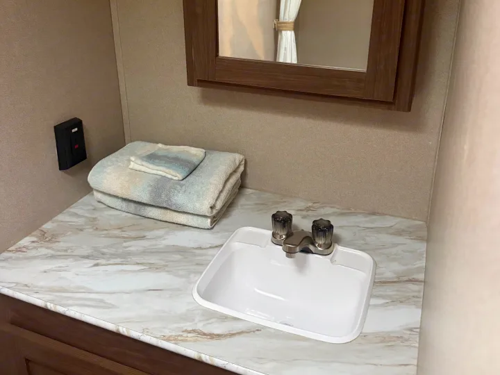 Compact RV rental bathroom vanity with sink, mirror, and towels, offering essential amenities for your trip.. Keystone RV Hideout 2020