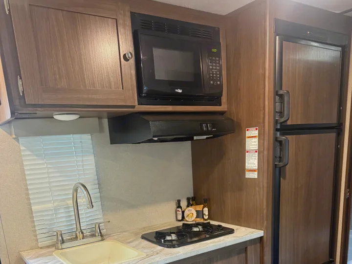RV rental kitchen featuring a microwave, range hood, stove, sink, and refrigerator, surrounded by wood-look cabinets.. Keystone RV Hideout 2020