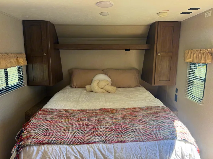 Inviting RV rental bedroom with a cozy bed, ample overhead storage, and natural light from windows. Ready for rest!. Keystone RV Hideout 2020