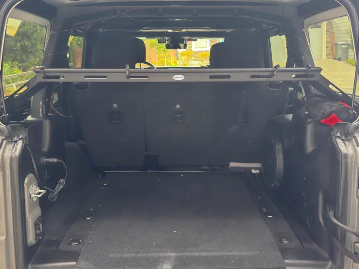 Rear cargo area of a vehicle, possibly for an rv rental, featuring fold-up seats, carpeted floor, power outlet, and cargo bar.. Jeep Wrangler Rubicon Unlimited 2021
