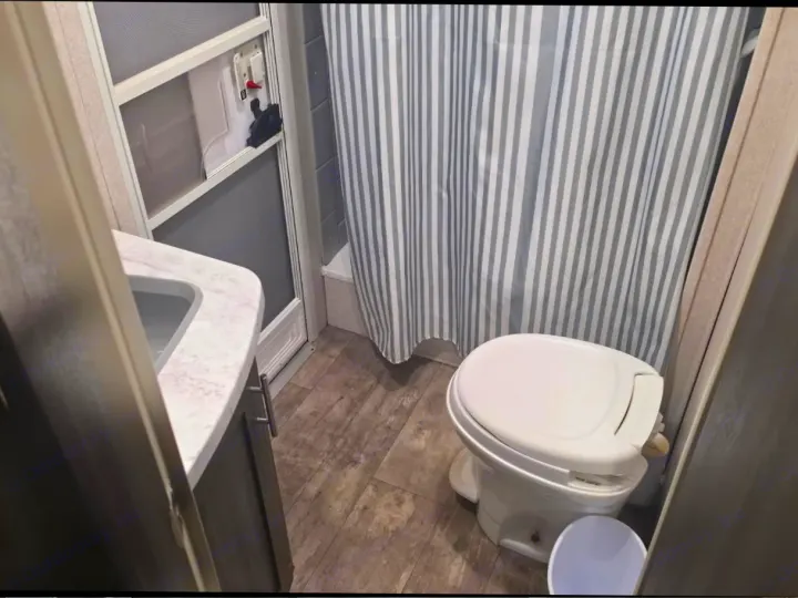 Compact RV rental bathroom features a toilet, shower with a striped curtain, and a small sink, showcasing its functional space.. Shasta Shasta 2020