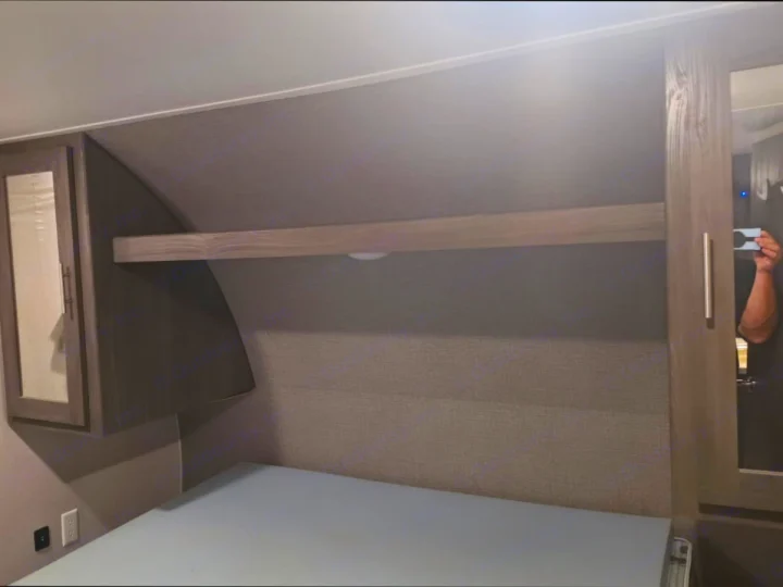 Cozy RV rental bedroom with light mattress, textured headboard, wood shelf, and mirrored cabinets for storage.. Shasta Shasta 2020