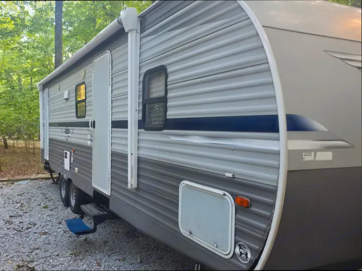 RV rental travel trailer parked at a tree-lined campsite, showing exterior details like steps, windows, and awning.. Shasta Shasta 2020